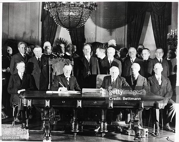 Washington, DC: President Calvin Coolidge signs the Kellogg-Briand Pact in his office. Secretary of State Frank B. Kellogg is seated to the left of...