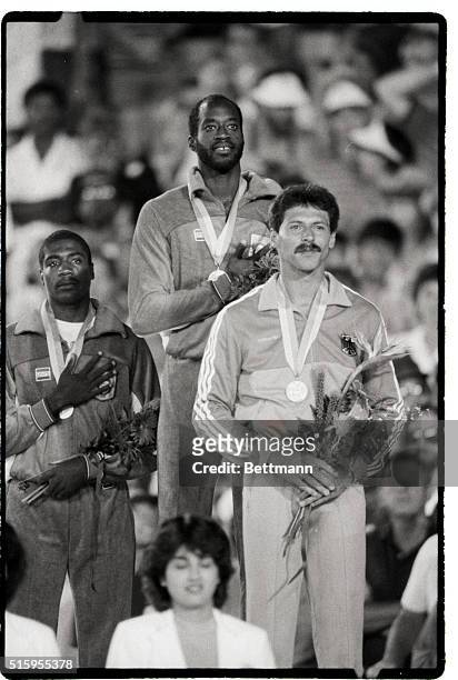 Americans Edwin Moses, gold medalist, and Danny Harris, silver medalist, put their hands over their hearts during the playing of the national anthem...