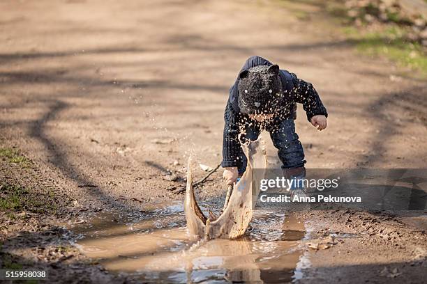 toddler boy with a stick playing ina puddle - eenjarig plantenkenmerk stockfoto's en -beelden