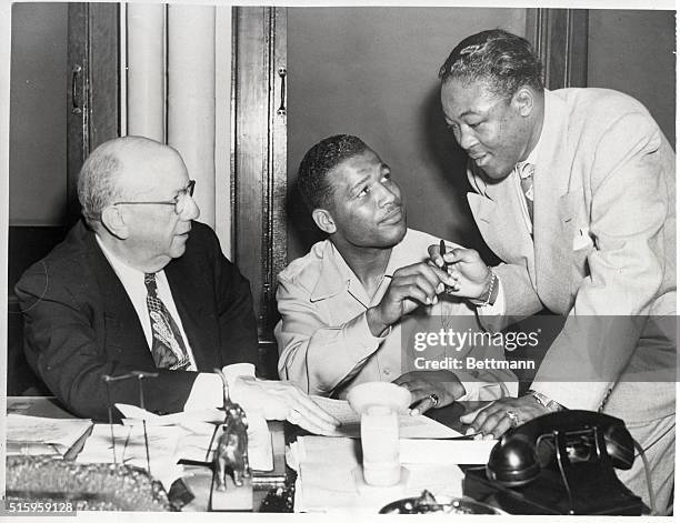 Philadelphia, PA- State Boxing Commissioner Leon Raines watches as welterweight champion Ray Robinson hands a pen to Cuban challenger Kik Gavilan....