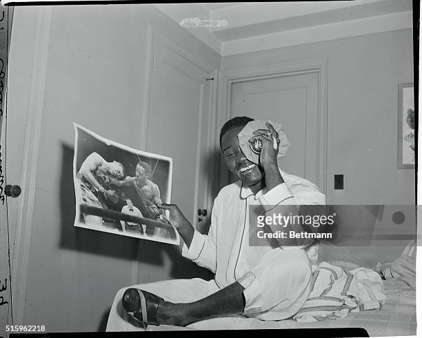 Cheerful eyeful on the morning after his Joe Louis fight, is heavyweight king Ezzard Charles, grinning at Hotel Edison, as he displays a fight photo...
