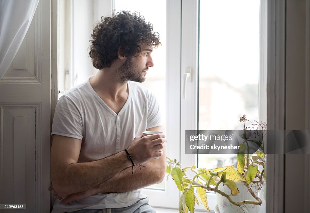 Pensive man with coffee cup looking through the window.