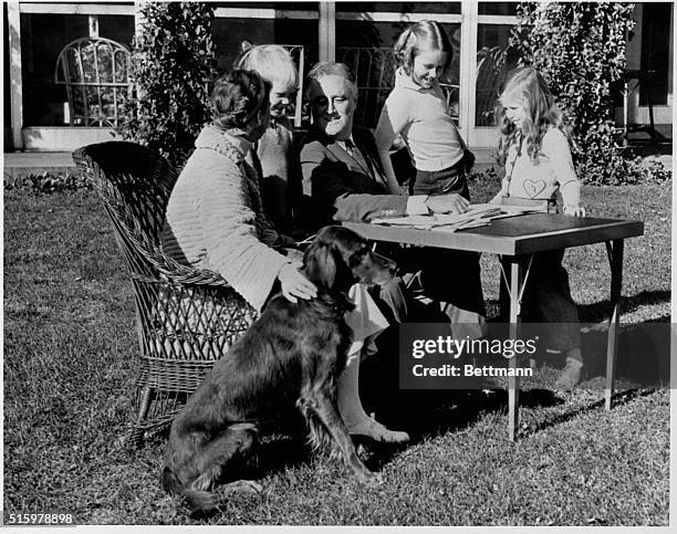 President Roosevelt and his family relax at their Hyde Park Estate. The president is sitting outside with his wife Eleanor and his grandchildren Anna...