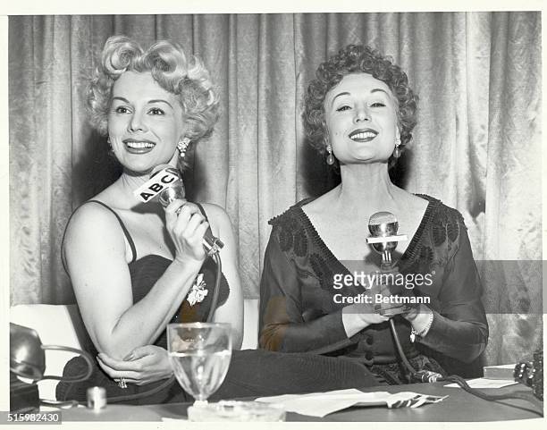 Eva Gabor, holding ABC microphone, sits next to her sister, Magda, who also holds a microphone. Photograph circa the late 1950s.