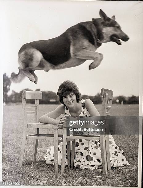 London, England- With a graceful arch, Sergeant of Barnhill leaps over his smiling mistress, 15-year-old Carole Mutter of London. The skillful German...