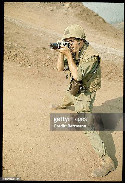 Dak To, South Vietnam: A newsphoto cameraman is shown taking a picture while standing on a dirt road. He is there with the soldiers of the 173rd...