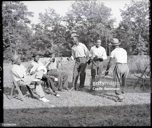 Group of African American men playing banjo and dancing on grass.