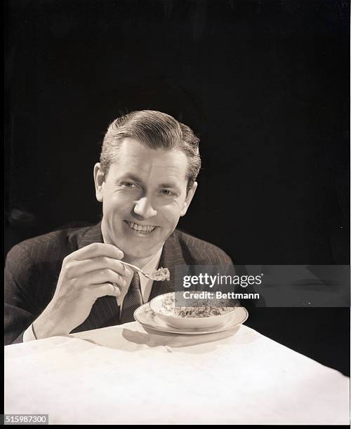 Carefully groomed man in a pinstriped suit eats from a bowl of raisin bran. Undated photograph.