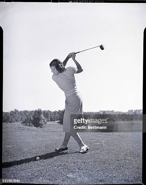 Woman prepares to make a fairway wood shot on a golf course. Photograph circa 1950's.