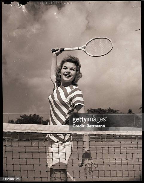 Muriel Smith plays tennis close to the net, her racket held high.