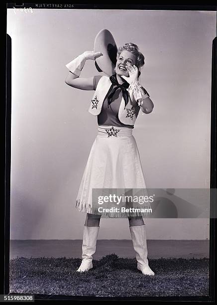 Photo shows a woman dressed as a cowgirl, yelling with her hands by her mouth. Model: Betty Jane Hess. Ca. 1940s.