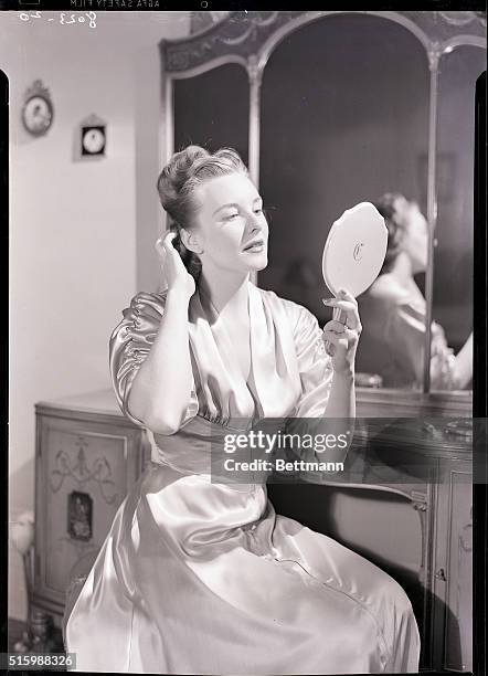 Barbara Lewis pats her hair as she primps in her bedroom. She looks into a handheld mirror. Ca. 1945-1960.