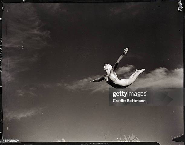 Picture shows a below shot of a woman diving gracefully in the air. Her arms are spread out wide and she has on a bathing suit and swimming cap. The...