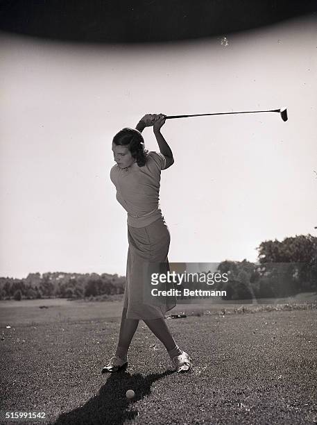Photo shows a young woman about to swing a golf club at a golf ball on the ground. Model: Blanche Fennell. Ca. 1950s.