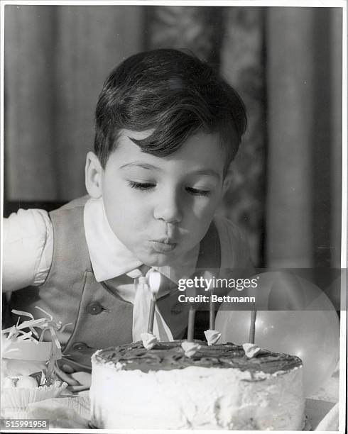 Young boy blows out four candles on his birthday cake. Undated photograph, circa 1950.