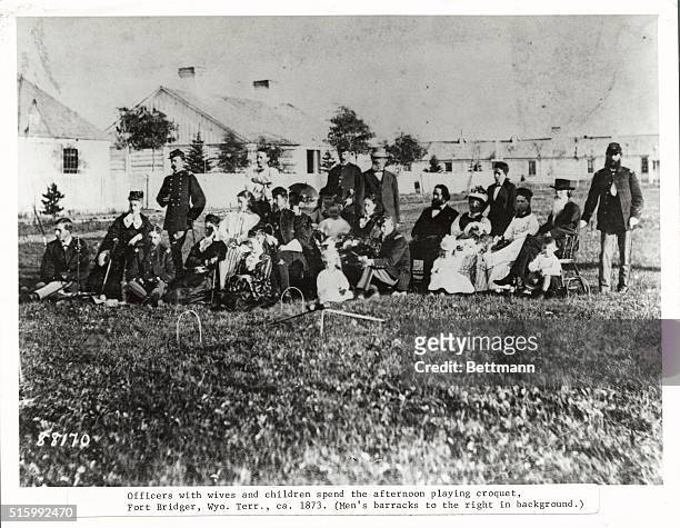 Officers with wives and children spend the afternoon playing croquet at Fort Bridger, Wyoming Territory. The men's barracks are to the right in...
