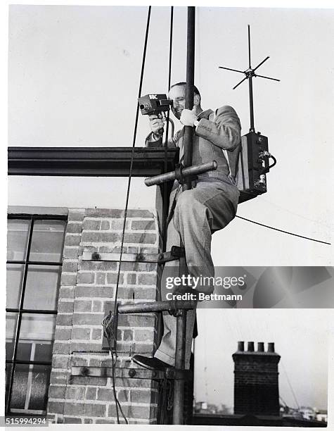 London, England- Clambering up a flagpole, British boradcaster Brian Johnston takes a bird's eye view of London with a small portable television...