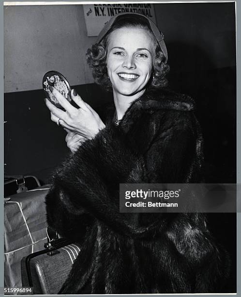 British actress Honor Blackman , smiles and holds a compact. She wears a fur coat and is surrounded by suitcases. Undated photograph.