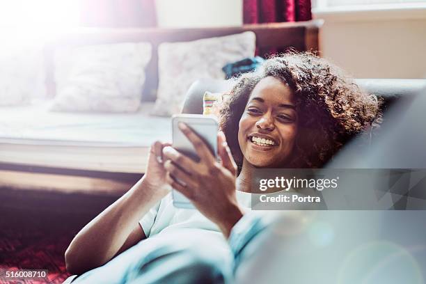happy woman using mobile phone on sofa - kleine scherptediepte stockfoto's en -beelden
