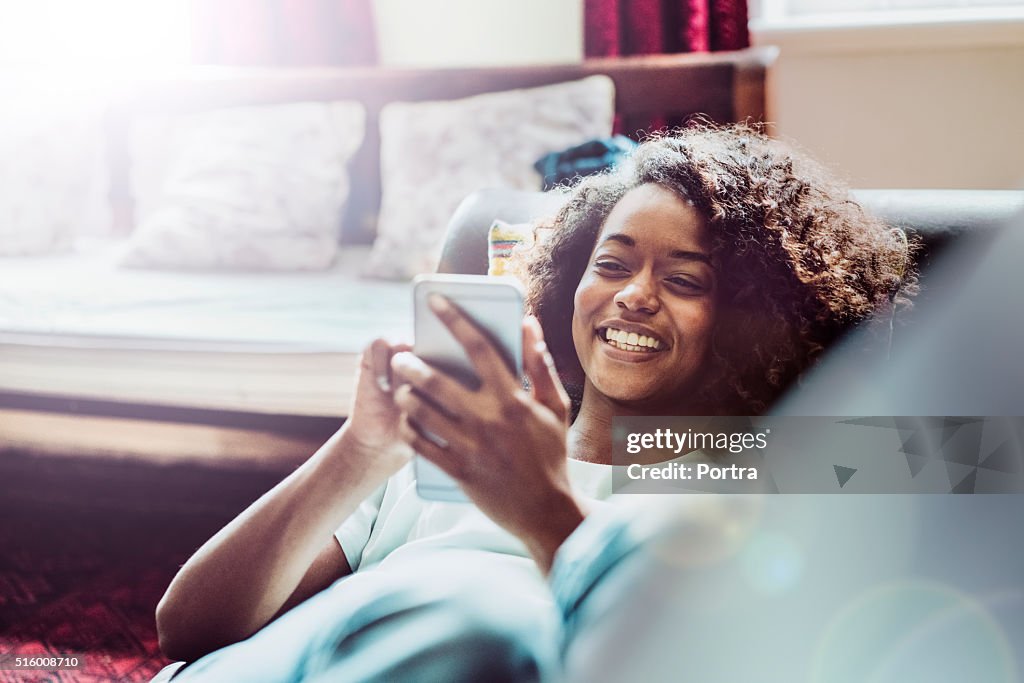 Happy woman using mobile phone on sofa