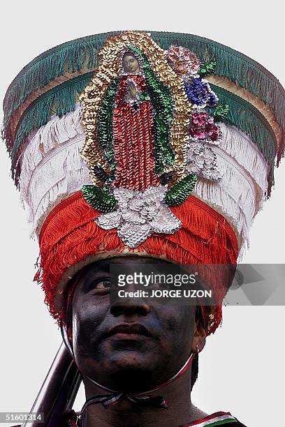 Man, with his face painted in black, is dressed like a Mexican Indigenous soldier and wears a hat with the image of the Virgin of Guadalupe, during...