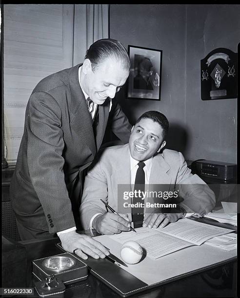 Brooklyn Dodgers vice president Buzzie Bavasi looks on as pitcher Don Newcombe signs a contract to remain with the team. 1951.