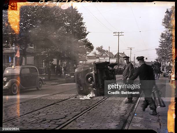 Cleveland, OH-A policeman looks on while a fireman rushes with an extinguisher to attempt salvage on the car overturned and set on fire during the...