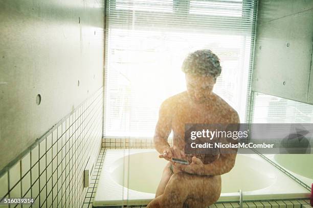 man using mobile phone on edge of bath tub - minimalist living in japan stock pictures, royalty-free photos & images