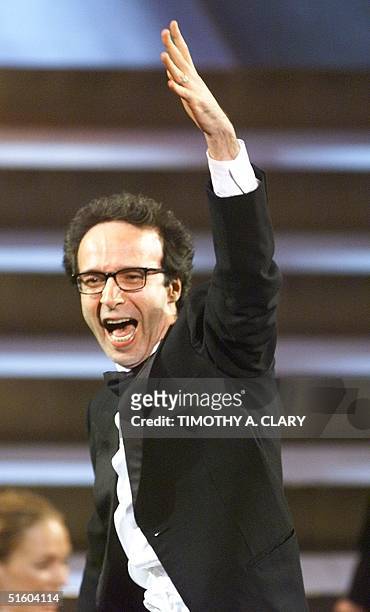 Italian director Roberto Benigni stands in his chair and celebrates after winning an Oscar for Best Foreign Language Film for his movie "Life is...