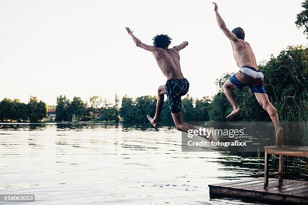 carefree summer day: teenagers jumping into a lake - locs hairstyle stockfoto's en -beelden