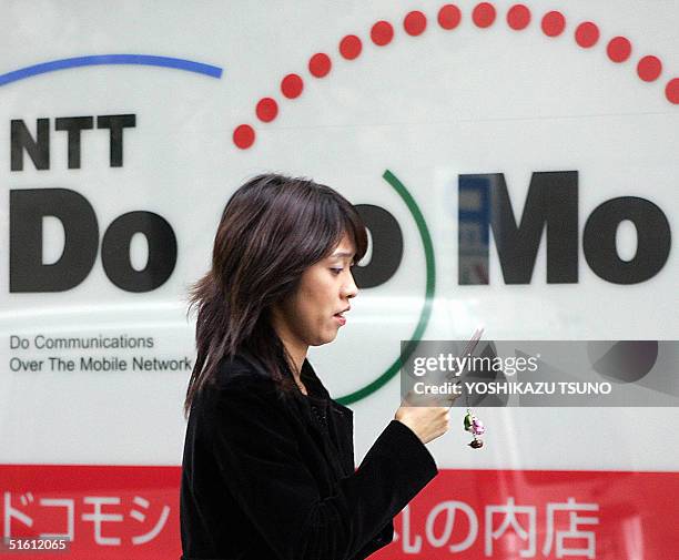 Woman browses her mobile phone as she walks past a NTT DoCoMo shop in Tokyo, 29 October 2004. Japan's top mobile phone operator NTT DoCoMo said its...