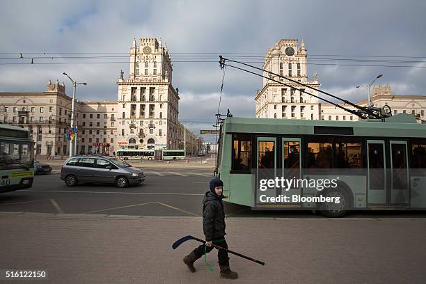 Boy carries his ice hockey stick along a sidewalk past the Gates of Minsk, center, in Minsk, Belarus, on Wednesday, March 16, 2016. European Union...