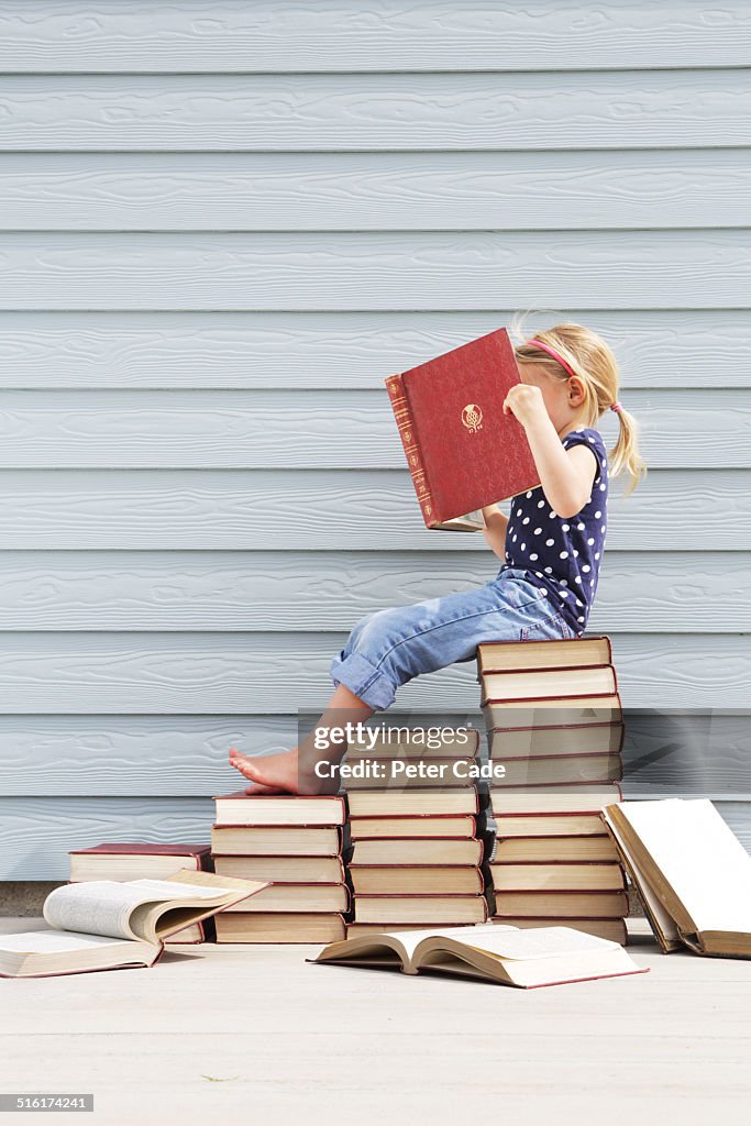 Girl sitting on pile of books .Girl reading book