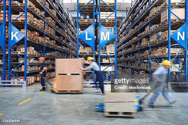 coworkers carrying cardboard box in warehouse. - industrial warehouse stock pictures, royalty-free photos & images