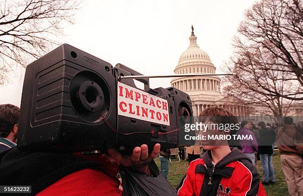 Man shoulders a portable radio with the words "Impeach Clinton" pasted on its side as the US House of Representatives votes on the articles of...