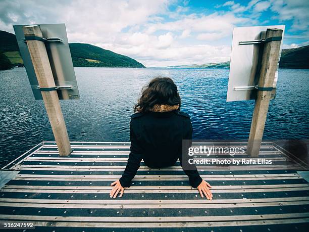 woman sitting on dock in front of loch ness (scotland) - female looking away from camera serious thinking outside natural stock pictures, royalty-free photos & images