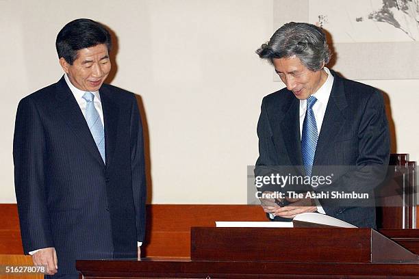 Japanese Prime Minister Junichiro Koizumi signs the visitors' book while new South Korean President Roh Moo Hyun watches during their bilateral...