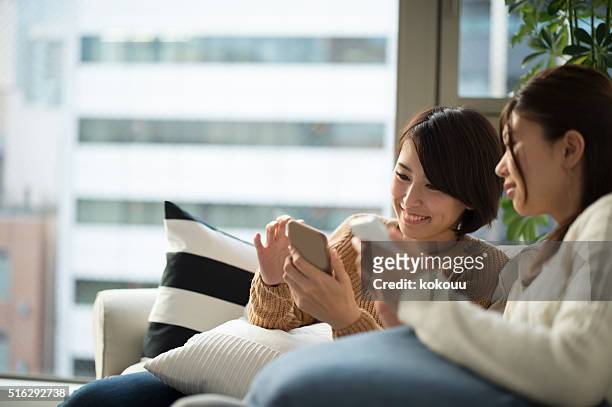 women who have seen friends and smartphone on the couch - picture magazine stockfoto's en -beelden