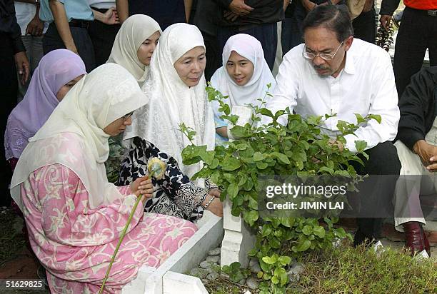 Former deputy prime minister Anwar Ibrahim sits at his father's grave accompanied by his wife Wan Azizah and daughters after arriving in Kuala...