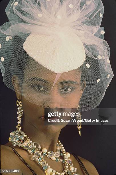 Headshot portrait of an unidentified model, in a hat with pink, tulle netting, and a variety of costume jewellery, 1976. This image was taken as part...