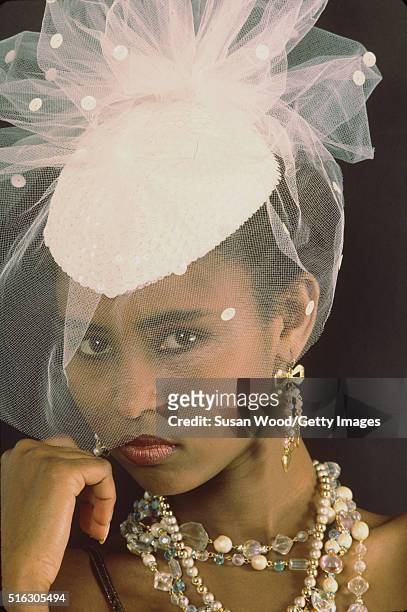 Headshot portrait of an unidentified model, in a hat with pink, tulle netting, and a variety of costume jewellery, 1976. This image was taken as part...