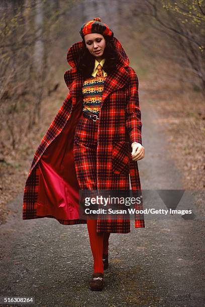 Portrait of an unidentified model in a red plaid coat and hat as she walks along a wooded road, 1972. This image was taken as part of a fashion shoot.