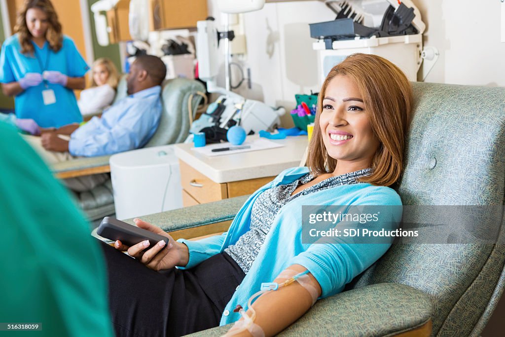 Hispanic woman donating blood in busy hospital donation bank