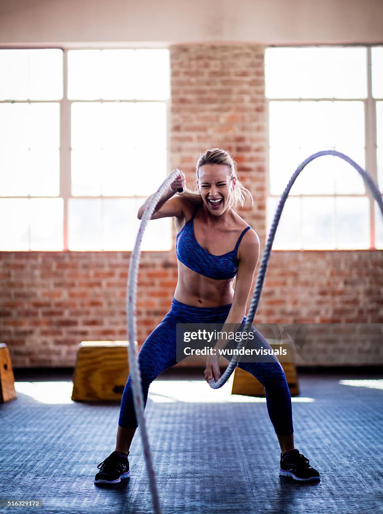 Athletic girl efforting on gym training with ropes at gym