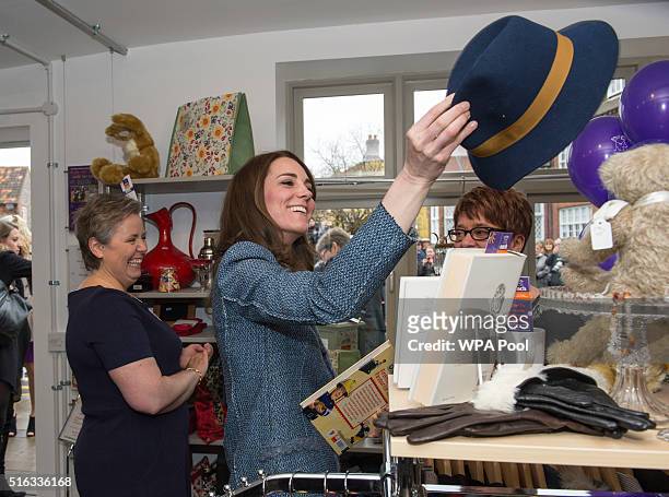 Catherine, Duchess of Cambridge tries on a Boden hat, priced at £15, as she takes a tour of the new EACH charity shop that she officially opened...