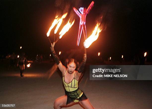 Woman dancing with fire on her fingers nails in front of the neon-lit Burning Man statue 06 September in the Black Rock Desert in northwestern...