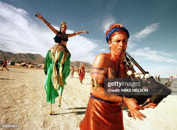 Bagpipe player and a belly dancer on stilts, participants in the "Burning Man" festival, cross a section of the Black Rock Desert 06 September in...