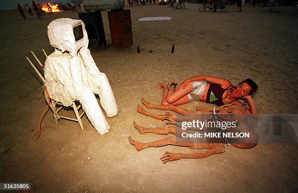 Woman lies next to paper mache aliens as they watch a television sculpted into a man 06 September at the "Burning Man" festival in the Black Rock...