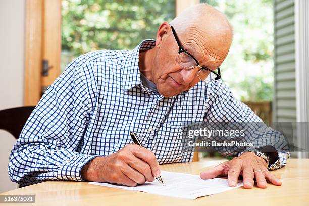 senior man filling out paperwork, signing document - holding pen in hand stock pictures, royalty-free photos & images