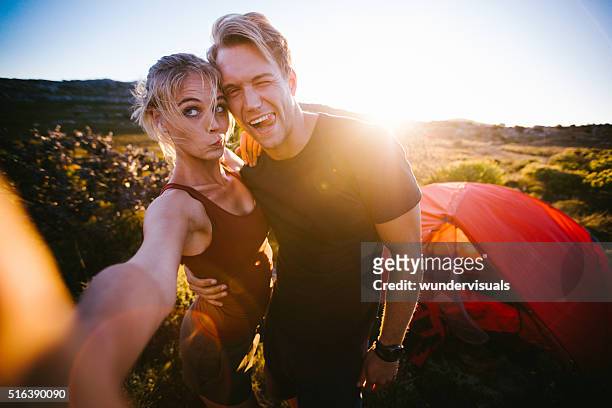 outdoor couple taking sunset selfie while camping on hiking vaca - funny selfie stockfoto's en -beelden